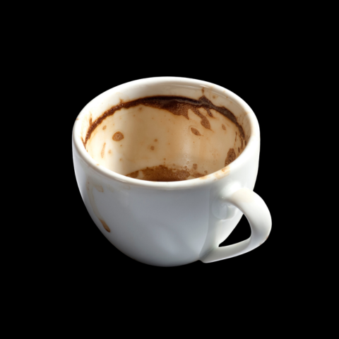 Splash of brewed organic coffee beans in a handmade cup on a neutral background
